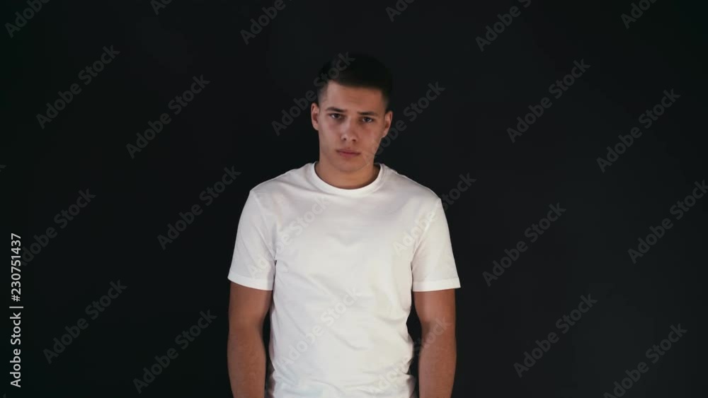 Very sad and serious young man stands straight and looks at camera. He express one emotion and it is sadness. Guy is very upset. Isolated on black background Very sad and serious young man stands straight and looks at camera. He express one emotion and it is sadness. Guy is very upset. Isolated on black background