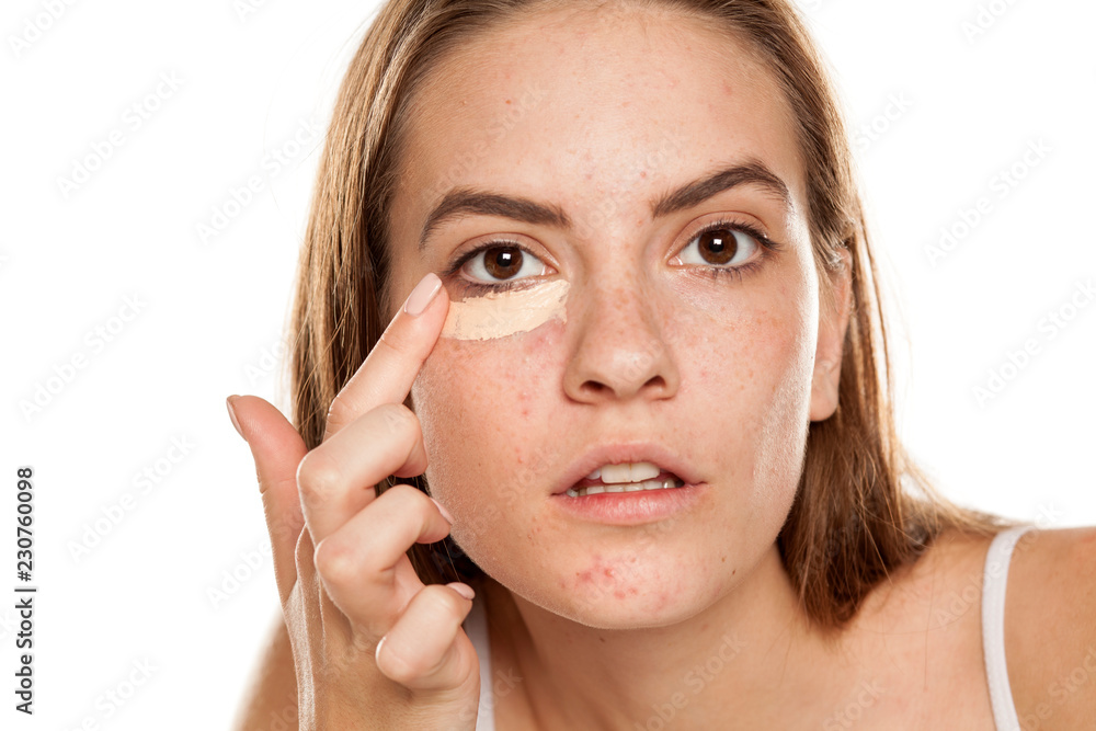 young beautiful girl applying concealer with fingers under her eyes on white backgeound young beautiful girl applying concealer with fingers under her eyes on white backgeound