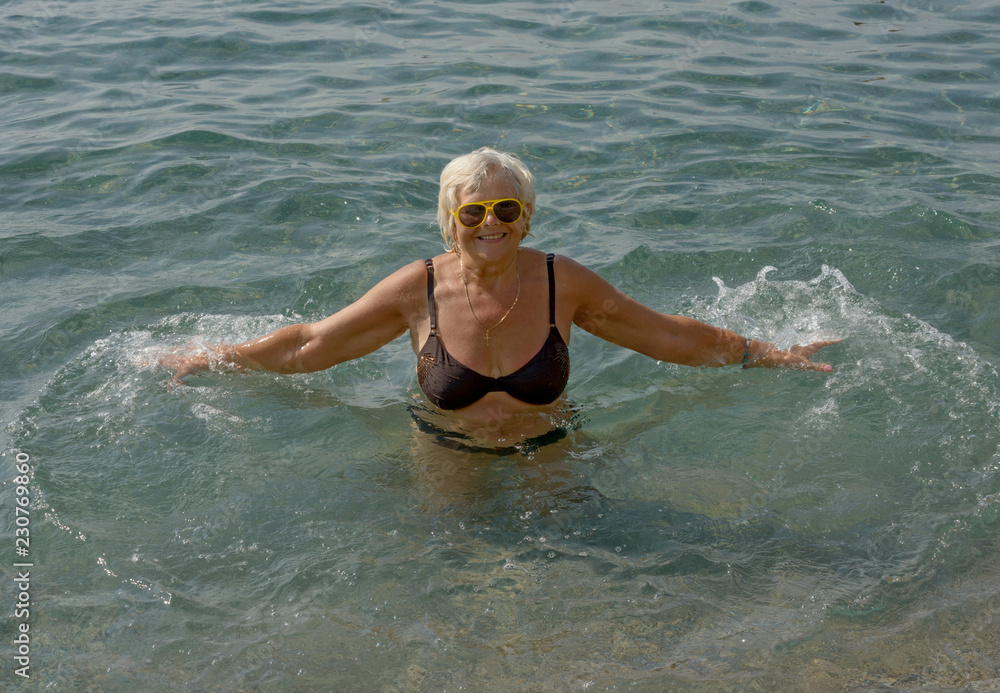 Aged woman is doing splashing motions in clear sea water.