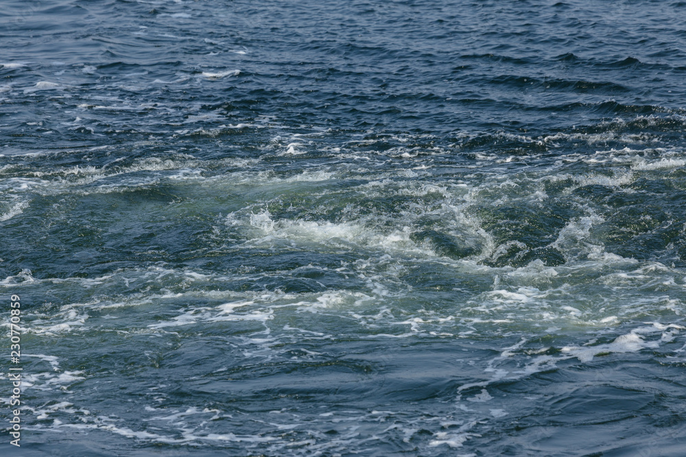 Track on the surface of the sea water behind the cargo sea ship. Trail on the surface of the water behind the speedboat. Sea wave trail on the surface, whirlpool, wave turbulence