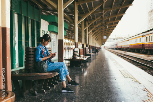 Asian woman traveler used smart phone while wait and check train schedule on the platform of the railway station - travel and transportation concept