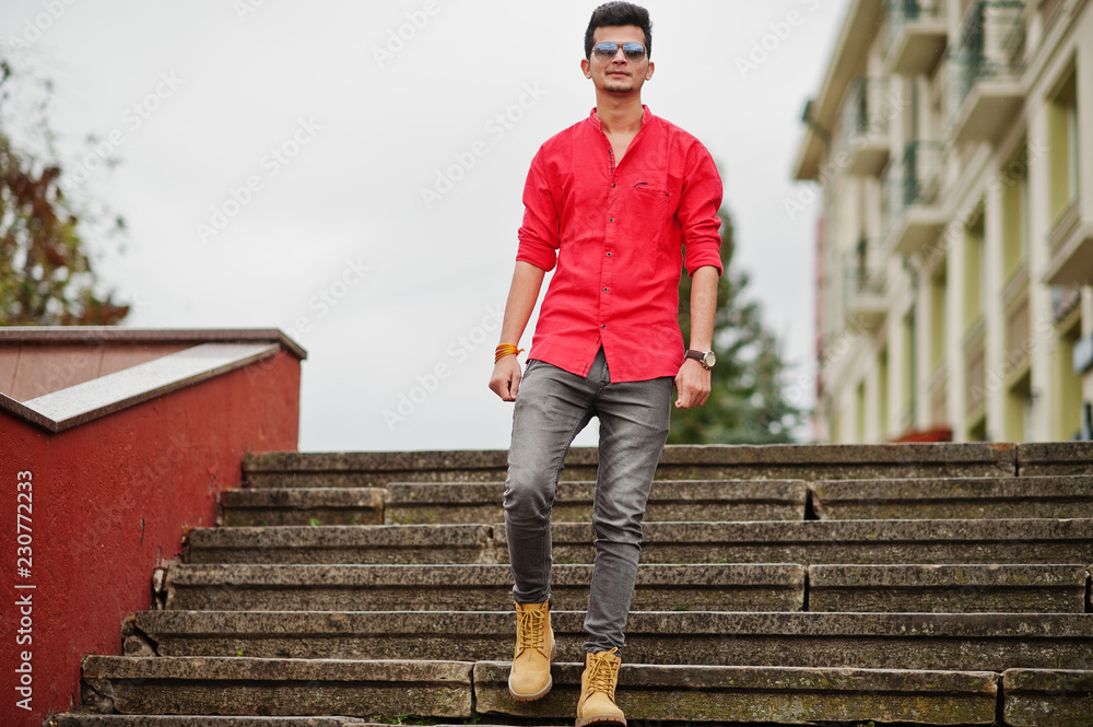 Indian man at red shirt and sunglasses posed outdoor.