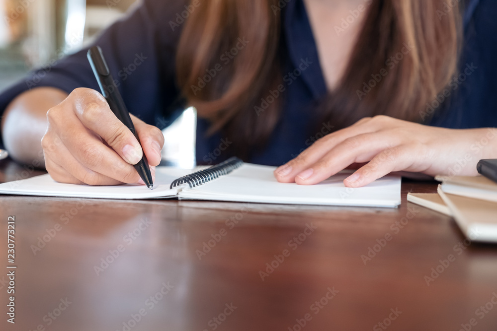 Closeup image of avwoman writing on blank notebook on table in cafe Closeup image of avwoman writing on blank notebook on table in cafe