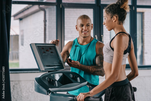 smiling african american male trainer with timer looking at sportswoman running on treadmill at gym © LIGHTFIELD STUDIOS