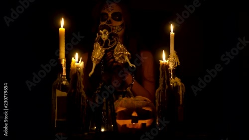 Halloween witch with skull makeup makes voodoo holds knife and wispering spell magic pumpkin chains and candles photo