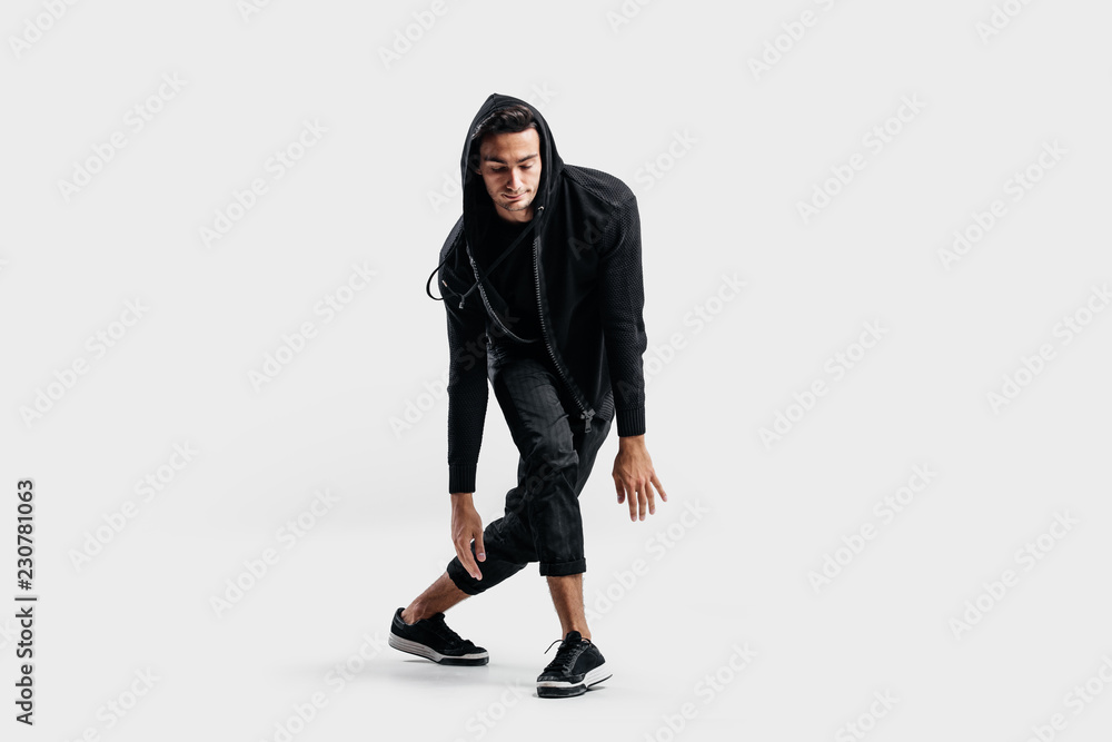 Dark-haired stylish dancer wearing black clothes and a hood makes stylized movements of street dance. Dark-haired stylish dancer wearing black clothes and a hood makes stylized movements of street dance.