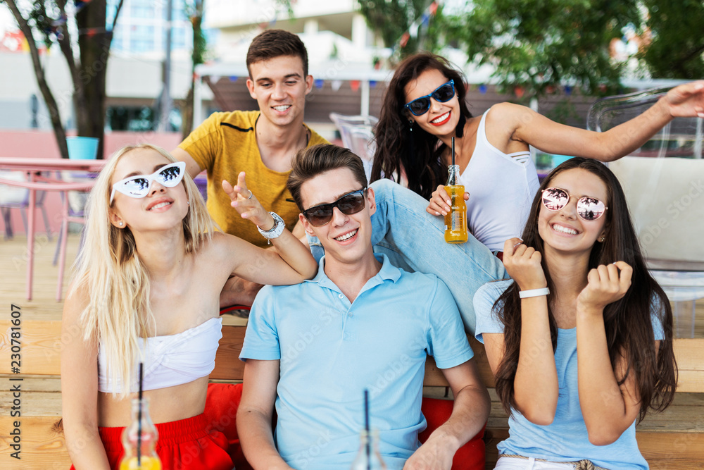 A company of good-looking friends wearing sunglasses laughing and drinking yellow cocktails and socialising at the table in the nice summer cafe. Cheers. Entertainment, having good time. Friendship. A company of good-looking friends wearing sunglasses laughing and drinking yellow cocktails and socialising at the table in the nice summer cafe. Cheers. Entertainment, having good time. Friendship.