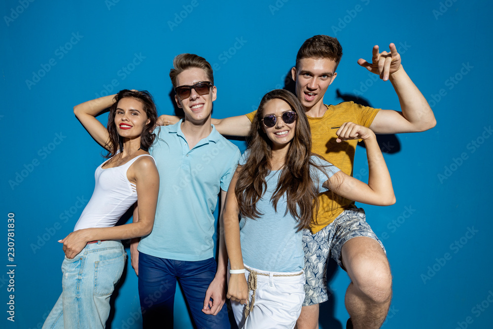 Four good-looking friends are laughing while standing in front of the blue wall having confident and happy looks. Entertainment, having good time. Friendship, relationship. Four good-looking friends are laughing while standing in front of the blue wall having confident and happy looks. Entertainment, having good time. Friendship, relationship.