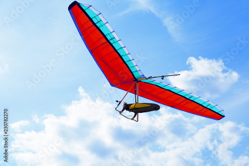 The hang glider on a red hang-glider is flying in a blue sky photo
