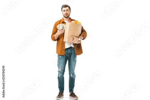 young man showing cash money and holding paper bag full of products isolated on white