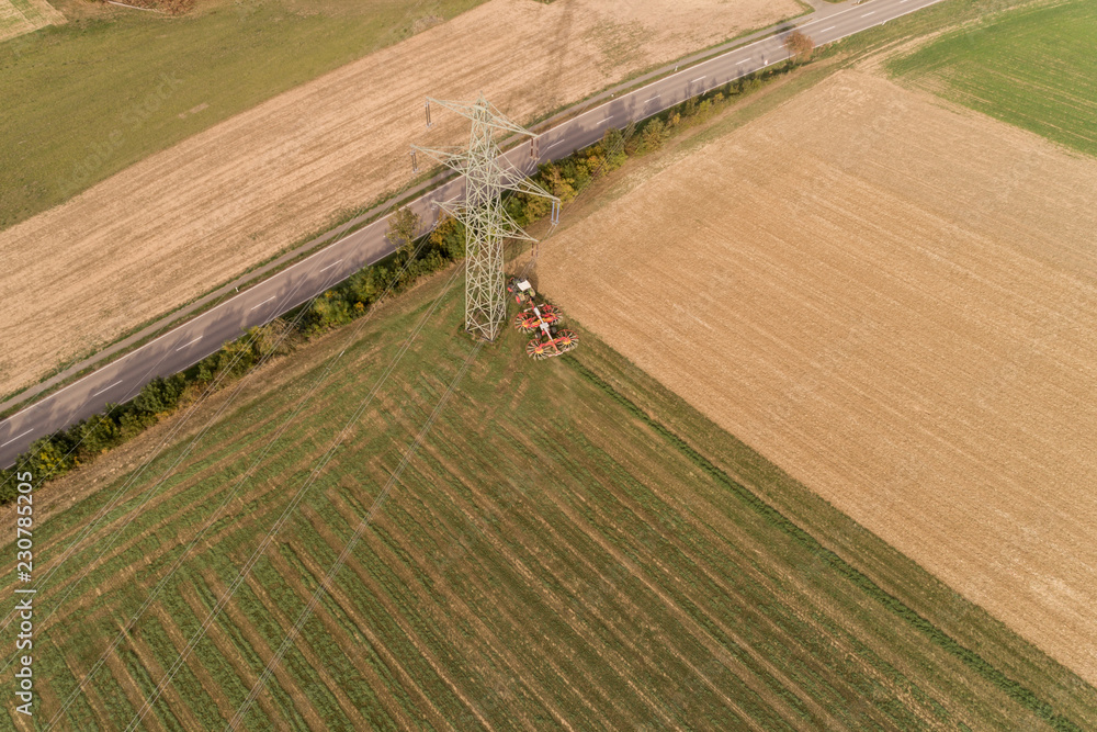 Bauer mit seinem Traktor bei der Grasernte am Fuße eines Strommasten