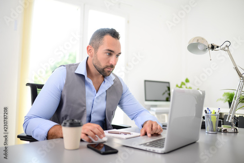 portrait of handsome trendy casual mid age business man in office desk with laptop computer