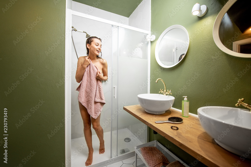 Young woman walking out from the shower cabin covered with a towel in