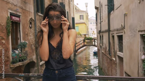Woman with carnival mask in Venice. Attractive young sensual romantic woman standing on the bridge against beautiful view on venetian chanal with boats and gondolas in Venice, Italy.