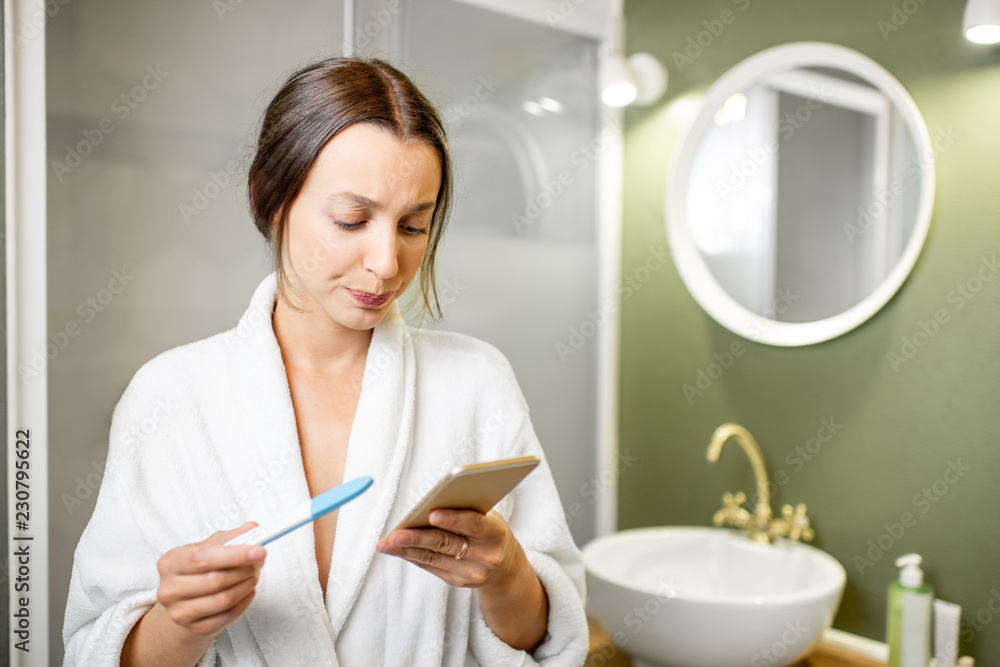 Sad and worried woman in bathrobe waiting for a result looking on a pregnancy test stick in the bathroom Sad and worried woman in bathrobe waiting for a result looking on a pregnancy test stick in the bathroom