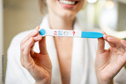 Happy woman holding pregnancy test stick in the bathroom. Close-up view focused on the stick