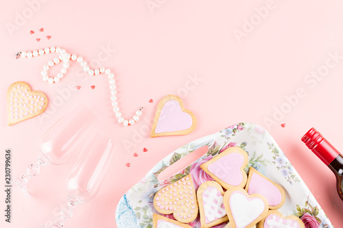 Valentine's day cookies, wine glasses and wine on pink background.