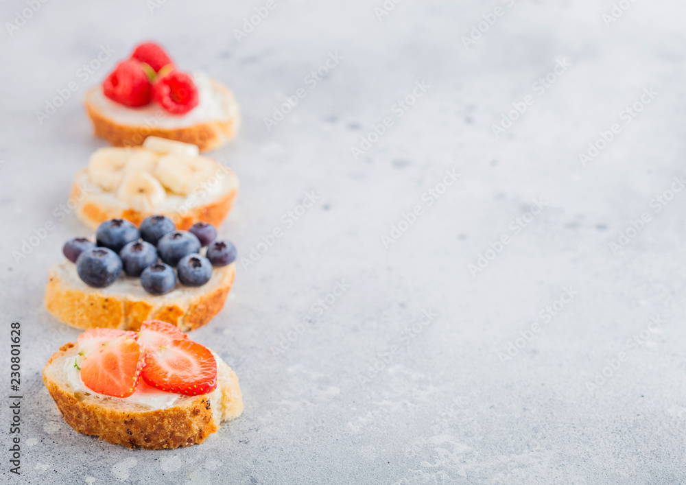Fresh healthy mini sandwiches with cream cheese, fruits and berries. Strawberries, blueberries, bananas and raspberries on stone kitchen table background. Space for text. Top view Fresh healthy mini sandwiches with cream cheese, fruits and berries. Strawberries, blueberries, bananas and raspberries on stone kitchen table background. Space for text. Top view