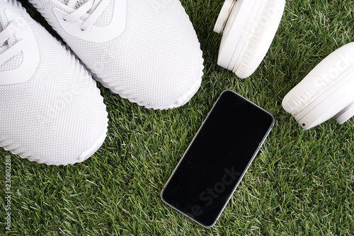 Fitness or healthy lifestyle concept. White running shoes, headphones and smartphone on a grass.