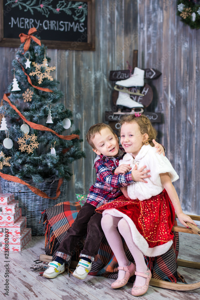 Φωτογραφία Two small children, brother and sister, are sitting on the background of the Christmas interior and gifts