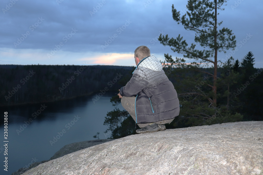 Fototapeta premium man sitting on a rock and looking at the lake