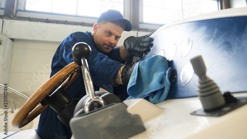 Young handsome professional guy (male) cleaner, washes the yacht after polishing and lining ceramics on the yacht. Concept of: Ceramics, Cleaning, New Ship, Polishing, Cleaner, In Robe, Cap, Hard Work