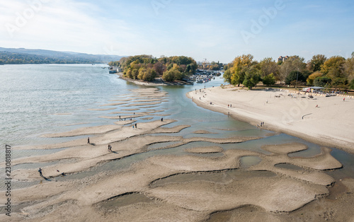 Low tide of the Danube river with people silhouettes walking on the sand islands left after water withdrawal in the Novi Sad, Serbia city beach