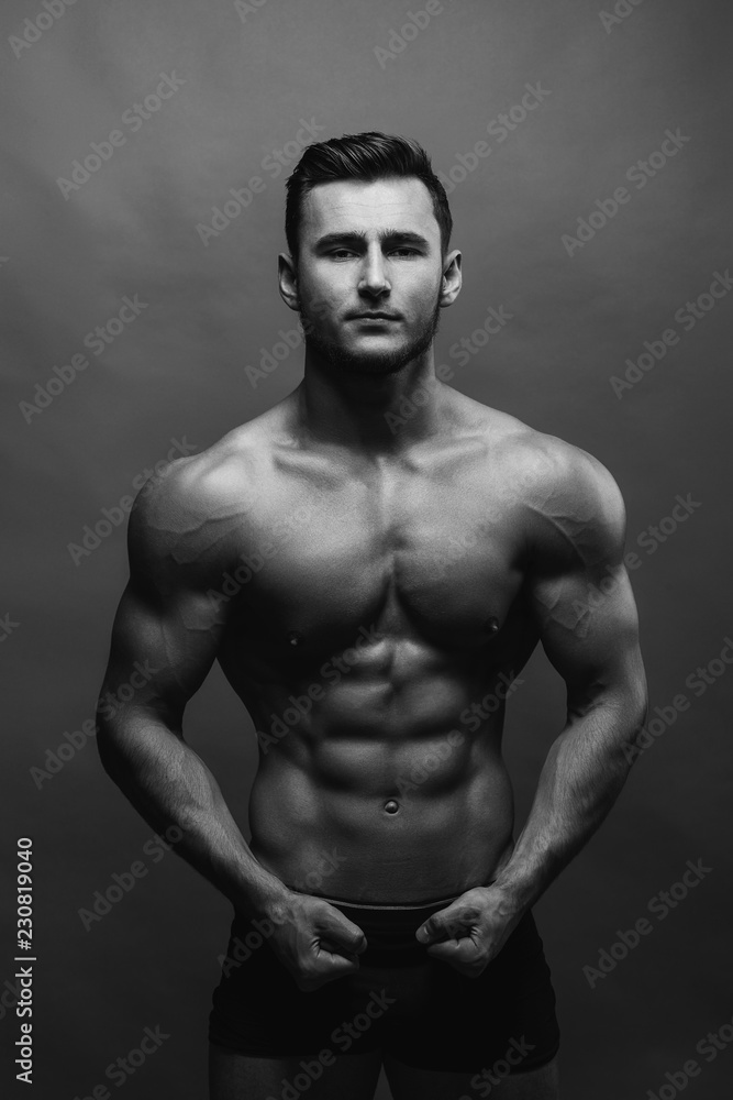 Bodybuilding. Strong man posing on background. Athletic young boy showing muscles.