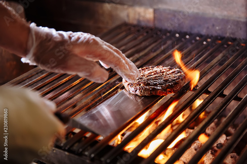 Chef making burger. Beef or pork meat barbecue burgers for hamburger prepared grilled on bbq fire flame grill. Close-up shot of chef's hands turn the chop on the grill