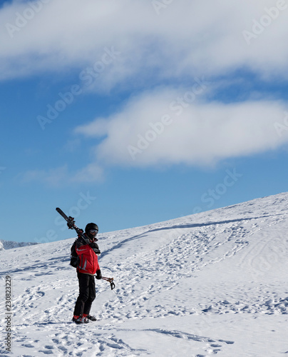 Skier with skis on his shoulder go up to top of mountain