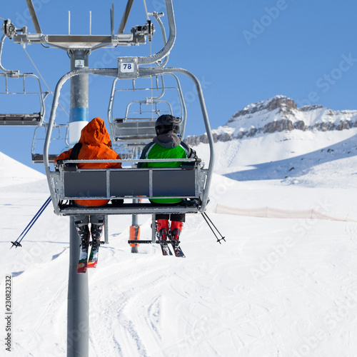 Two skiers on chair-lift and snowy ski slope photo