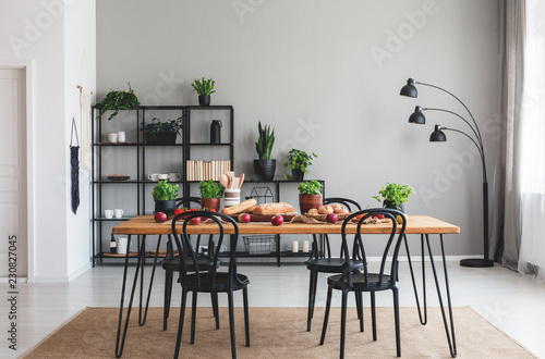 Black chairs and wooden table with food on brown carpet in grey dining room interior. Real photo