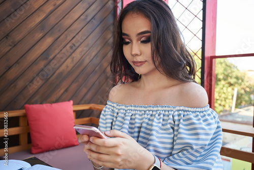 Beautiful smiling woman working on mobile phone. Attractive asian female is typing messages onmodern mobile phone. happy woman using laptop and smartphone in cafe photo