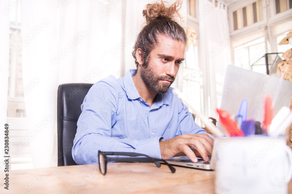 young man with long hair working with his laptop at home young man with long hair working with his laptop at home