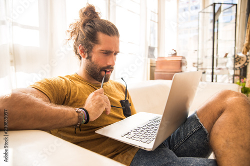 Quadro su tela man with long hair sitting on a sofa using his laptop