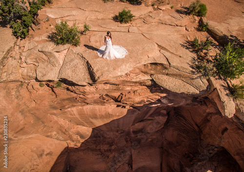 Aerial/Drone Wedding photo of a Bride in her wedding dress on a cliff overlooking a massive sinkhole in the Utah Desert, near Moab. photo