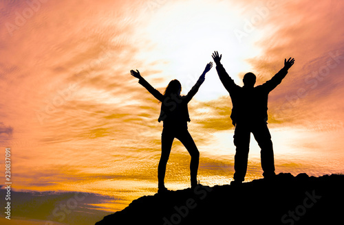 two people on top of the mountain holding hands up at sunset. achieving goals, winning, tourism, sports.