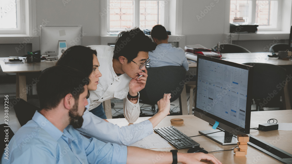Obraz premium Multi racial team of three office workers communicating together and discussing a project on a computer screen