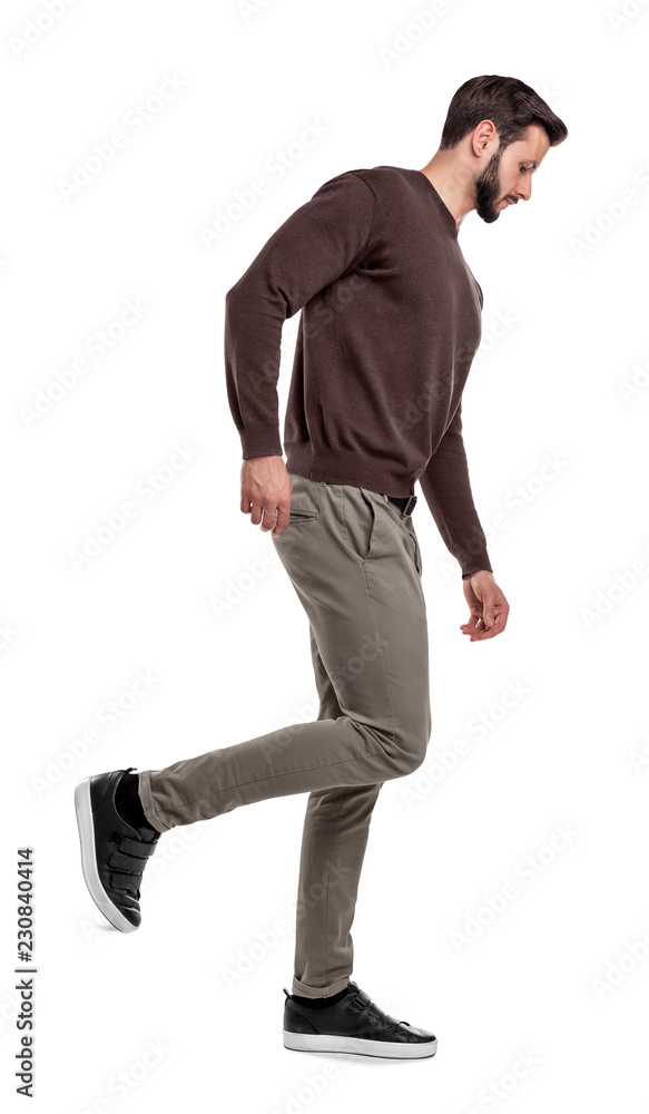 A serious looking man in casual clothes walks in a side view with one leg bent up behind him. A serious looking man in casual clothes walks in a side view with one leg bent up behind him.