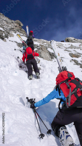 several backcountry skiers hike and climb to a remote mountain peak in Switzerland on a beautiful winter day