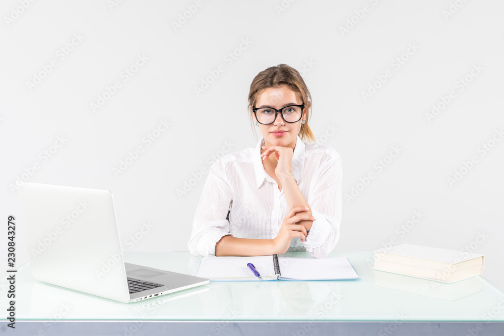 Young business woman sitting in front of a laptop with hands on chin at her office desk isolated on white background Young business woman sitting in front of a laptop with hands on chin at her office desk isolated on white background