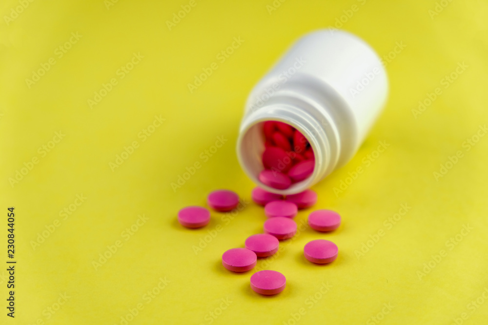 Bottle on its side with pink pills spilling out on yellow background. Bottle on its side with pink pills spilling out on yellow background.