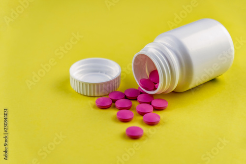 Bottle with cap on its side with pink pills spilling out on yellow background