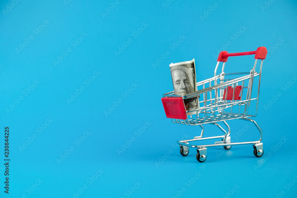 Shopping cart on blue background with  dollar bill. Symbol of consumerism.