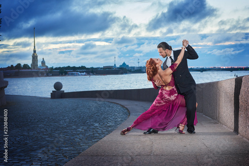 Young, beautiful and professional couple dancing tango on the quay of the river at daybreak in Saint-Petersburg on Peter and Paul Fortress and Neva river background