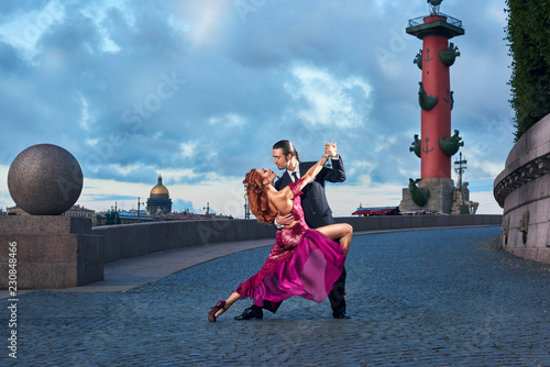Young, beautiful and professional couple dancing tango in Saint-Petersburg at Vasilyevsky Island on rostral columns background