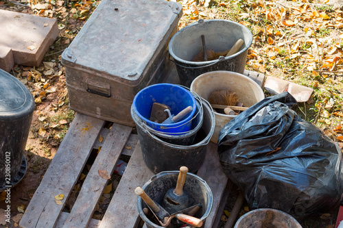 Old tools for construction sitting in the backyard. buckets, shovels, cement and garbage