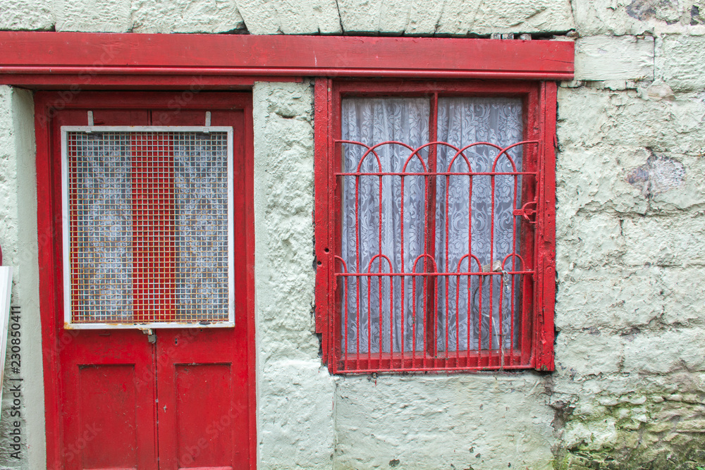 old red door and window with red iron work on a whitewashed stone house