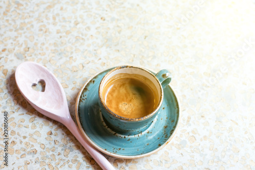 Modern blue coffee cup with wooden pink spoon with a heart in Cafe. View from above with copy space and toned with sunlight.