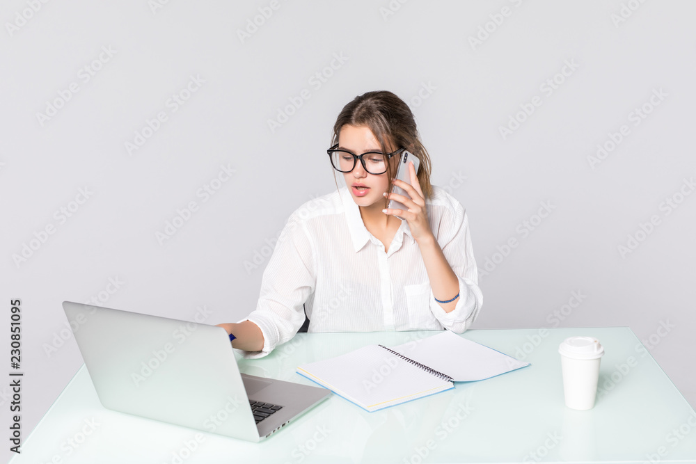 Beautiful young woman working on computer and talking on phone isolated on white background Beautiful young woman working on computer and talking on phone isolated on white background